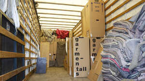 Inside a truck, there are boxes and stacked blankets.