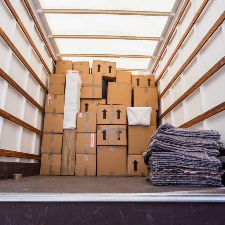 Person loading boxes into a truck on a street with houses in the background.