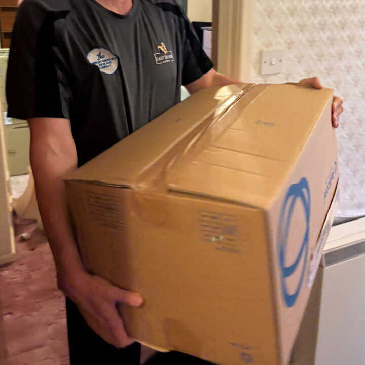 Two men are moving a large cardboard box from a vehicle.