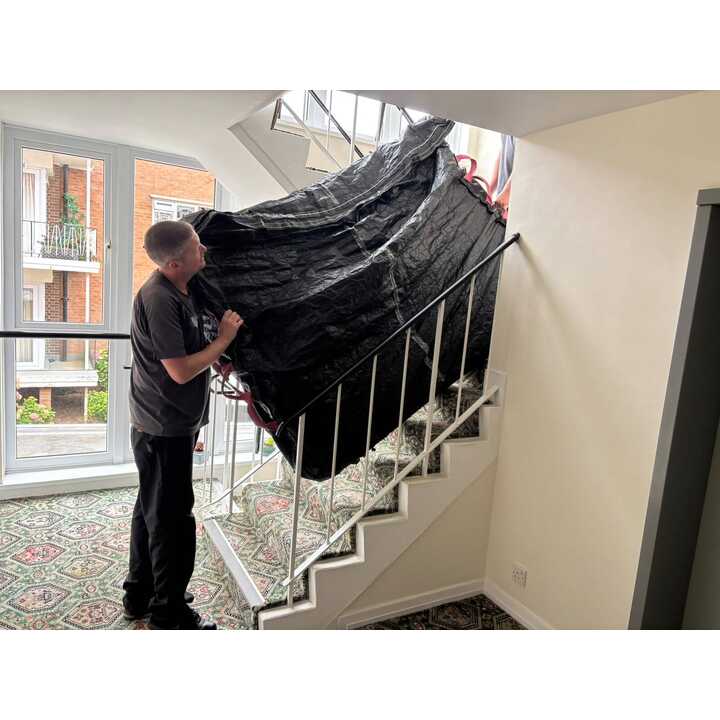 Removal company team member carrying a wrapped item down the stairs during a house move in East Devon