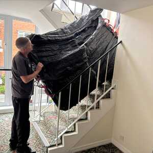 Removal company team member carrying a wrapped item down the stairs during a house move in East Devon