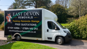 A removals van parked in a garden, featuring "East Devon Removals" on its side.