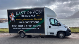 A white removal van with "East Devon Removals" written on the side, parked by a scenic landscape.