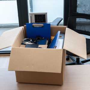 Open cardboard box on an office desk packed with a blue clipboard, cables and a desk phone