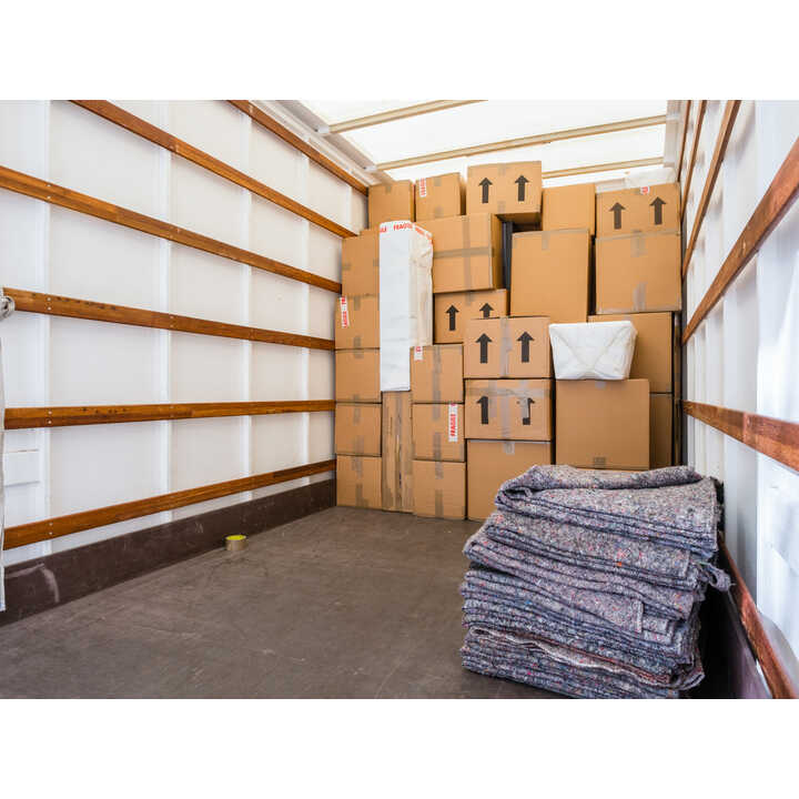 Cardboard boxes packed and labelled fragile inside a removal van, with a garment bag hanging alongside