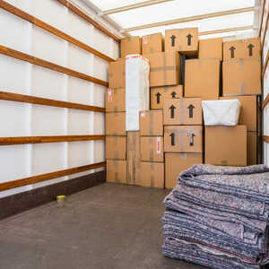 Cardboard boxes packed and labelled fragile inside a removal van, with a garment bag hanging alongside