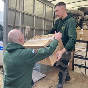 Two men are moving a large cardboard box from a vehicle.